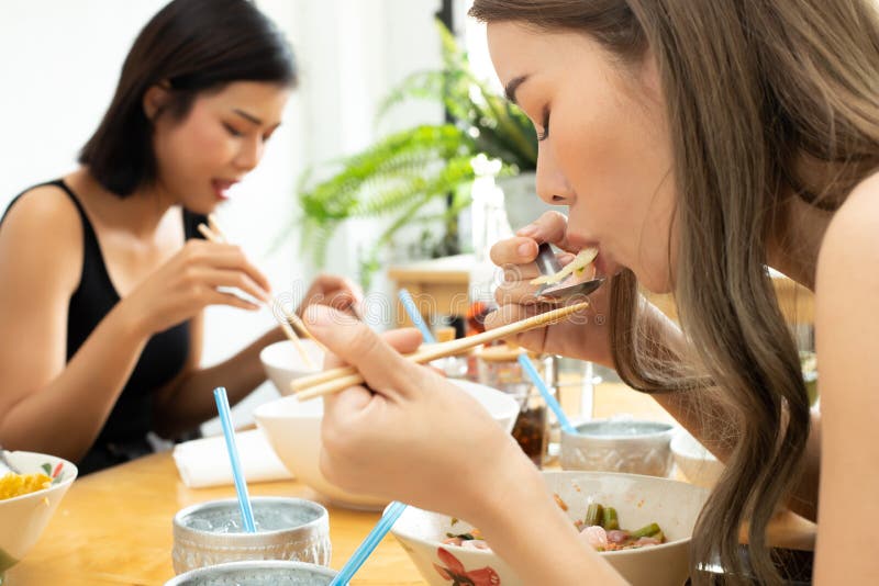 Young Asian Woman eats spicy hot tomyum noodle soup and hanging on chopstick to mouth with sweat delicious enjoy eating together