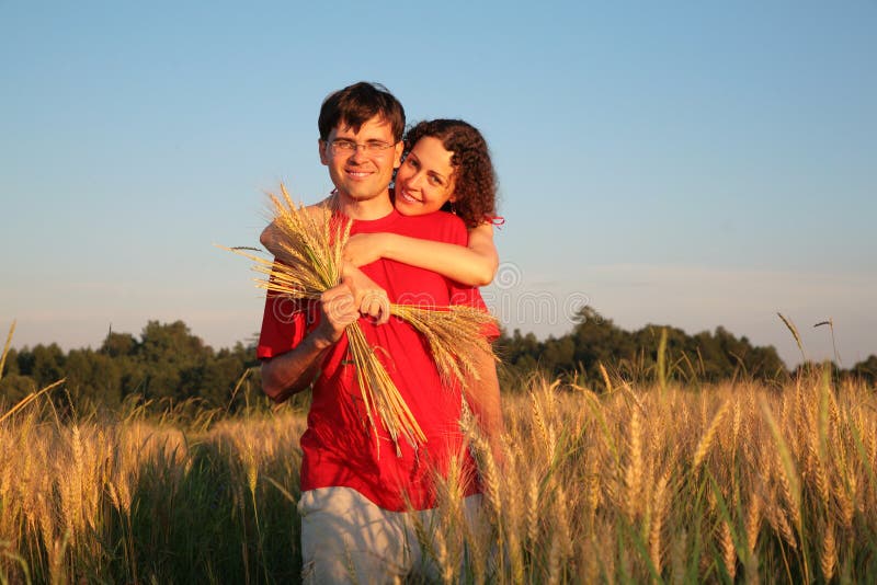 Woman embraces man behind on wheaten field