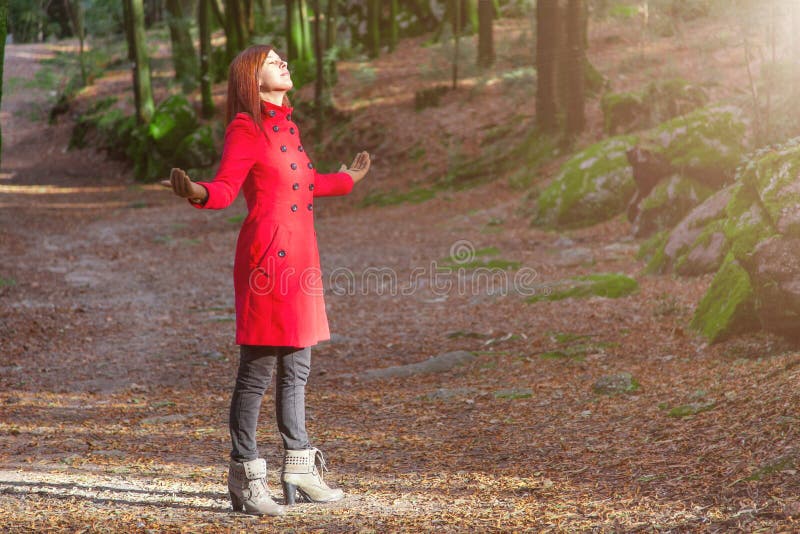 Woman enjoying the warmth of winter sunlight alone on forest park path with arms open