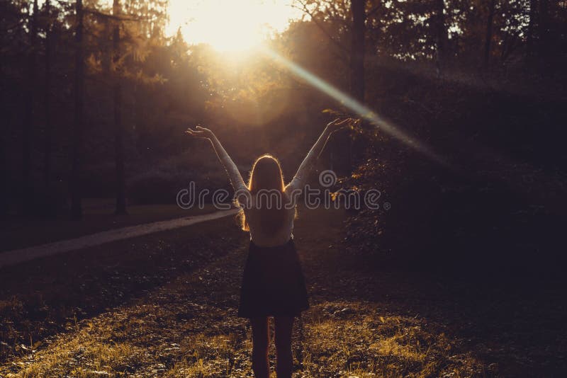 Woman feeling free on sunset. Silhouette of the woman spreading arms with her thumbs up, standing in forest in sunset light. Woman