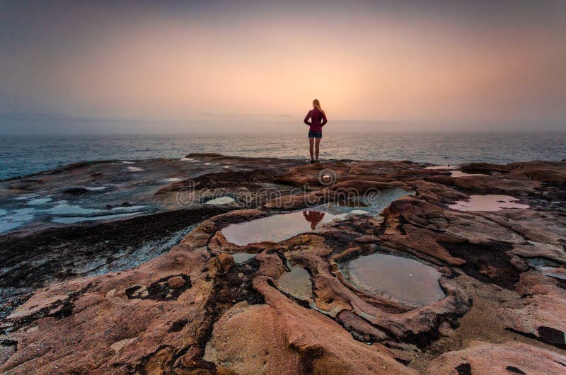 Woman standing on sandstone rocks with foggy coastal sunrise stock images Woman standing on sandstone rocks with foggy coastal sunrise stock images