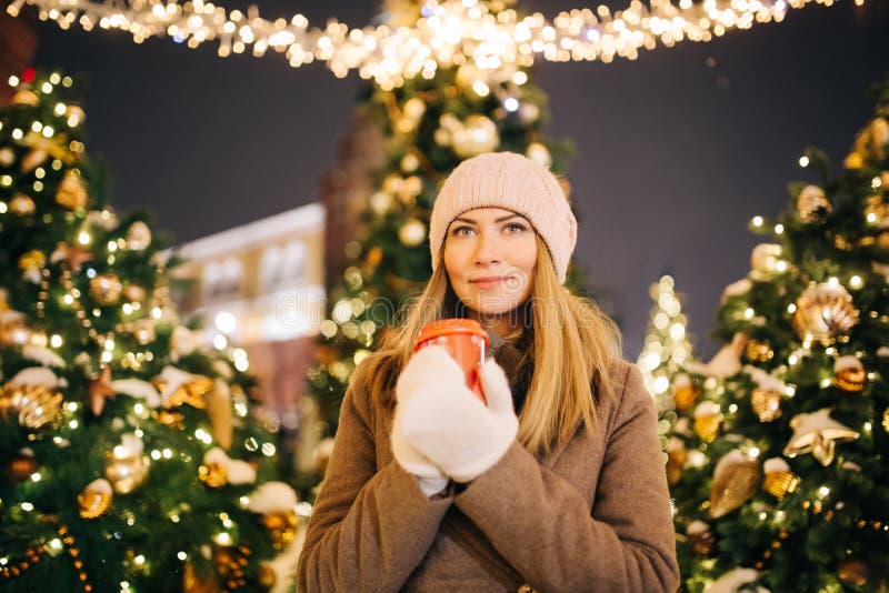 Woman with glass in her hands on street on background of fir trees with garlands. stock photography Woman with glass in her hands on street on background of fir trees with garlands. stock photography