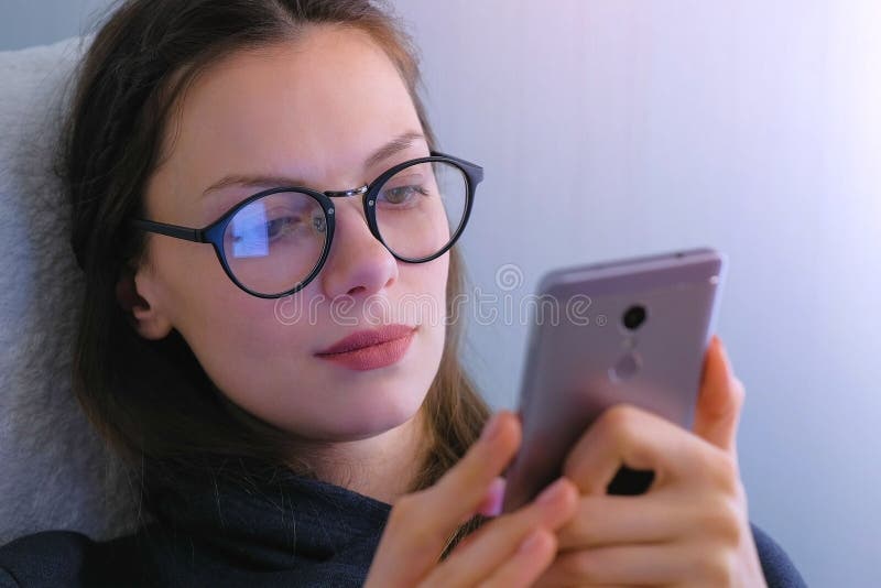 Woman in glasses watches serial on mobile phone. Face close-up.