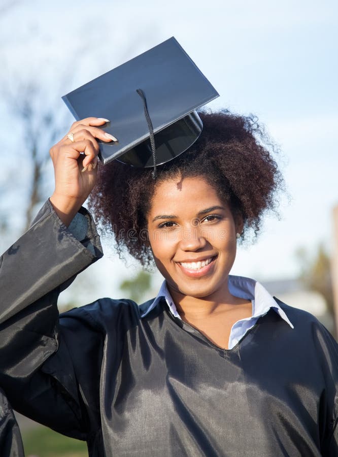 Smiling Student in Graduate Gown Holding Mortarboard · Free Stock Photo