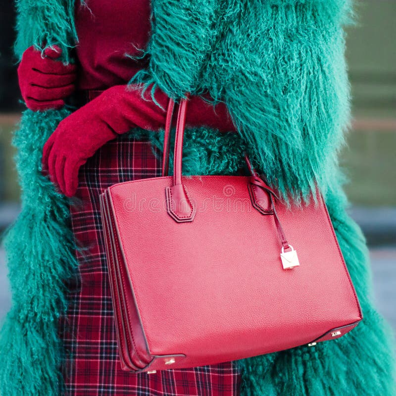 A woman in a green furry and warm fur coat in autumn or winter. Red burgundy bag. Fashionable bag close-up in female hands.