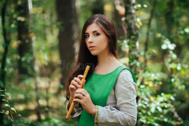 Woman in a Green Medieval Dress Plays the Wooden Flute while Standing in a  Grove Against the Background of Pines. Girl in a Gloomy Stock Image - Image  of forest, female: 188505231