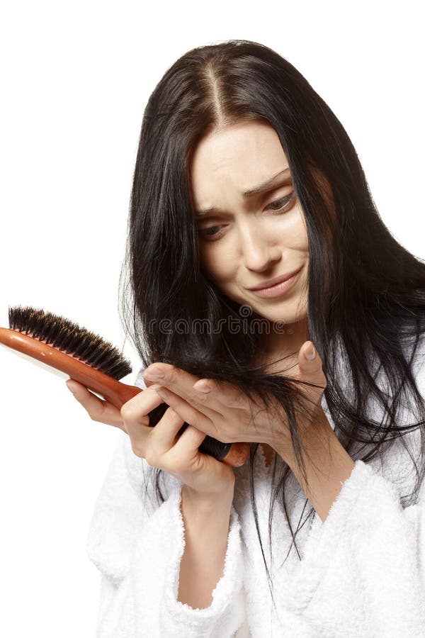 Sconvolto, il giovane donna in possesso di una spazzola per capelli in una mano e una manciata di capelli negli altri, isolato su sfondo bianco.