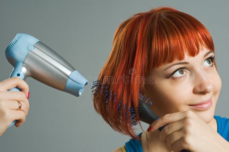 Woman with hairdryer and a hairbrush taking care of her red hair