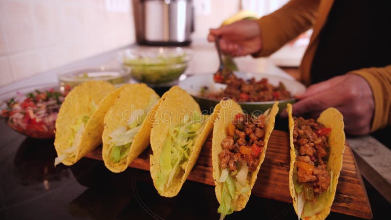 Woman hand adding the ground meat and vegetables filling to tacos
