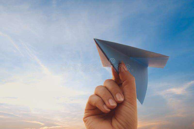 Woman Hand holding blue paper rocket with golden sky during sunset background. freedom concept