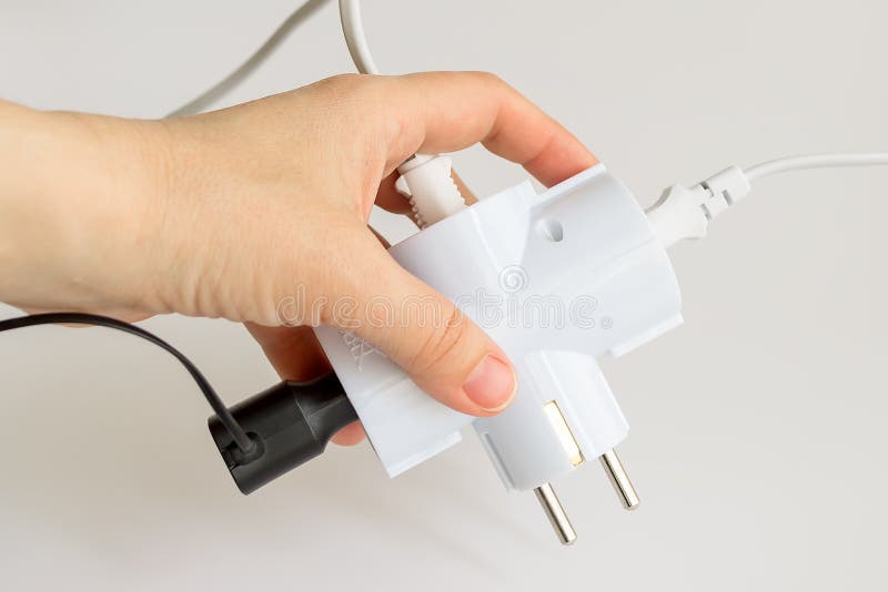Woman hand holding white electric splitter with tree plugs socketed into it on a white background. Splitter for simultaneous royalty free stock image