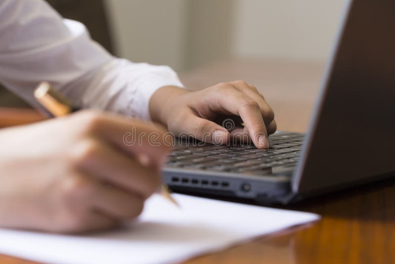 Woman hand writing a contract with a laptop beside