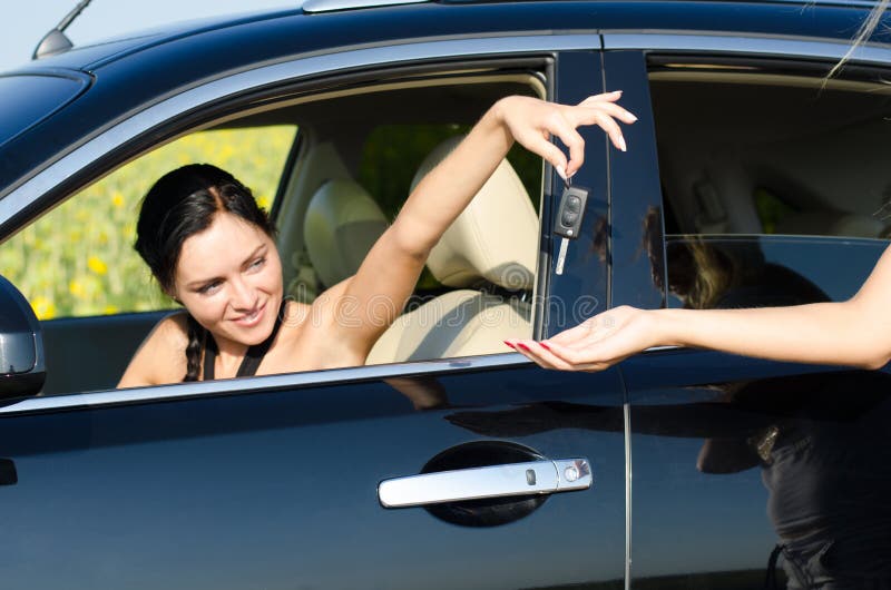 Woman driver handing over her car keys to a second woman standing outside the vehicle. Woman driver handing over her car keys to a second woman standing outside the vehicle