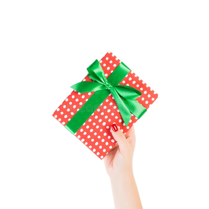 Woman hands give wrapped Christmas or other holiday handmade present in red paper with Green ribbon. Isolated on white background