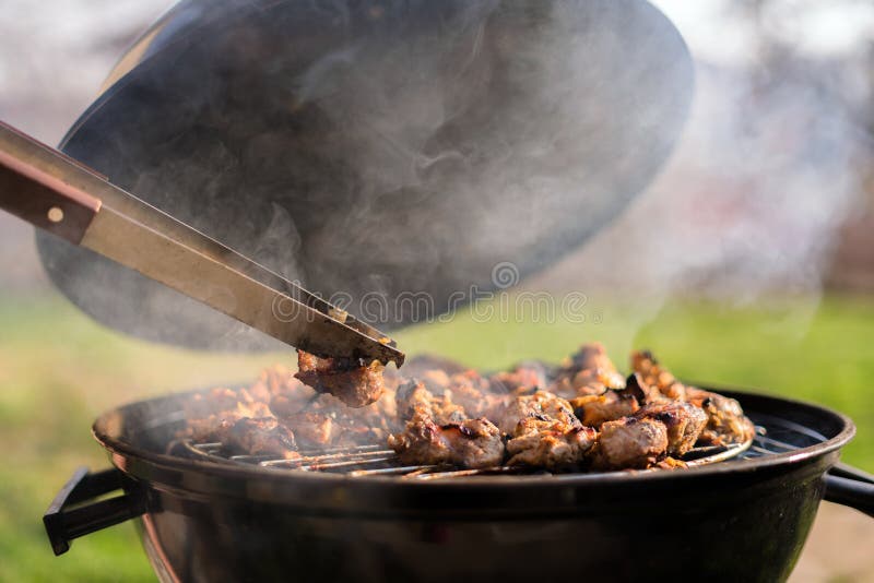 Woman hands grilling barbeque meet on the grill outdoors in the back yard. Summer time picnic. Roasting meat on metal grid on hot