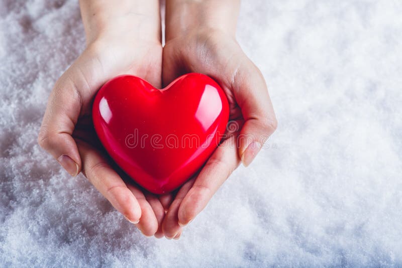 Woman hands are holding a beautiful glossy red heart in a snow background. Love and St. Valentine concept.