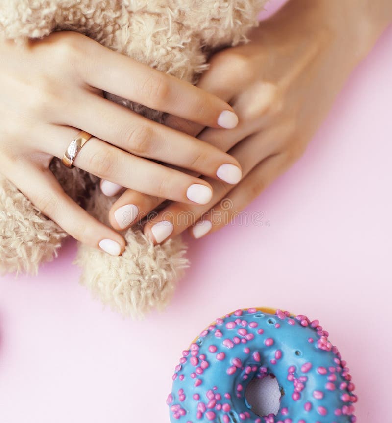 Woman hands with manicure wearing wedding ring holdind teddy bear and macaroons on pink background