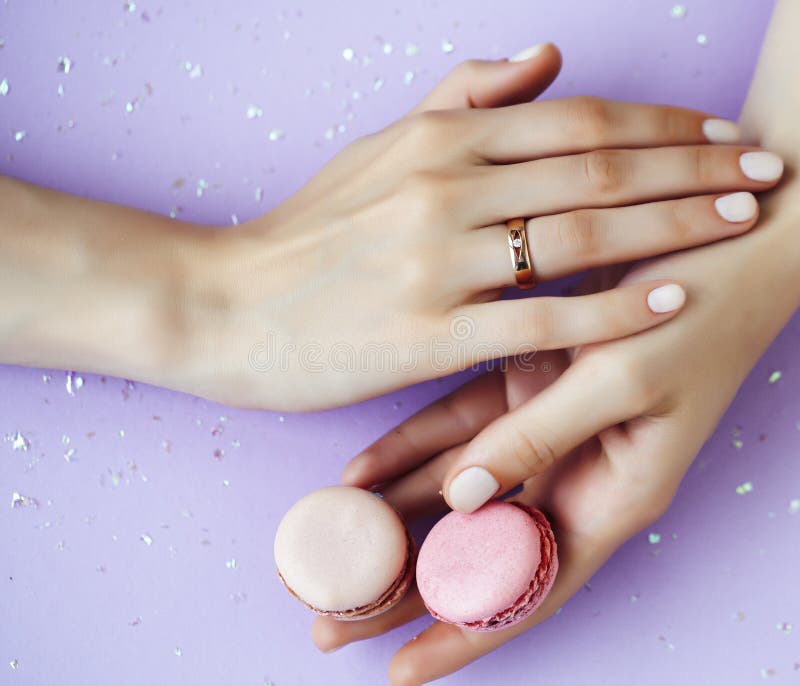 Woman hands with manicure wearing wedding ring holdind teddy bear and macaroons on pink background