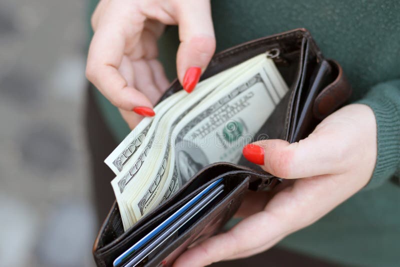 Woman hands with red nails holds black mens purse with many US hundred dollars bills. Concept of salary earnings or counting money