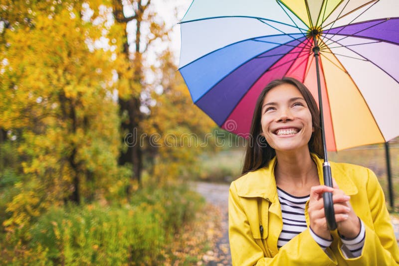 Woman happy with umbrella under the rain during Autumn forest walk. Girl enjoying rainy fall day looking up at sky