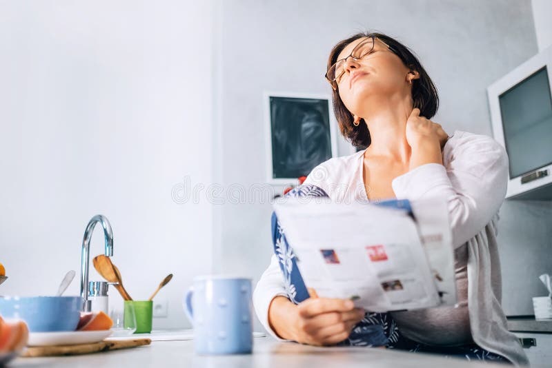 Woman has a neck pain when reads a magazine on the kitchen at mo