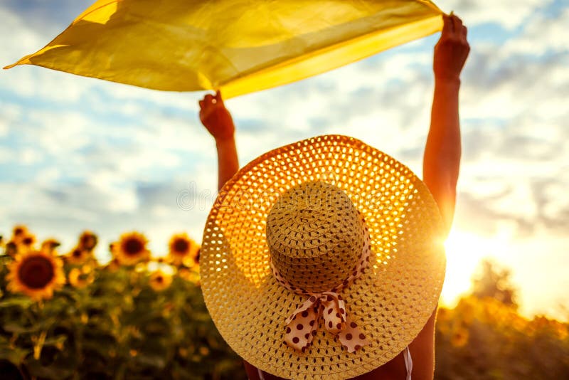 Woman in hat relaxing in blooming sunflower field raised arms with scarf and having fun. Free and happy. Summer vacation