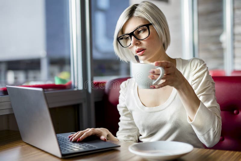 Young woman having coffee while working on laptop at table in cafe. Young woman having coffee while working on laptop at table in cafe