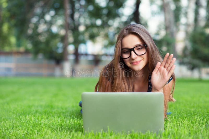Woman Having a Video Call with a Laptop and Headphones Outside in Park Lying Down Stock Photo