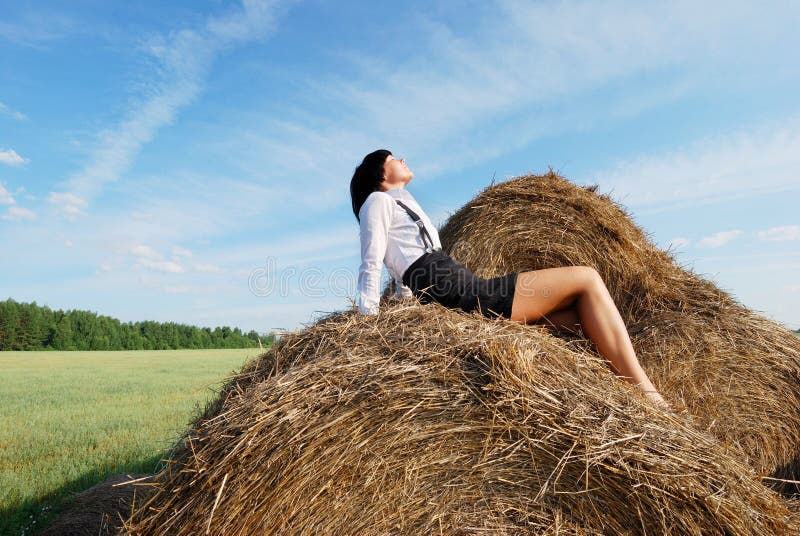 Woman on hay bale in summer field enjoying a warm windy day