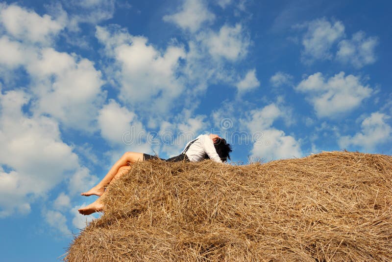 Woman on hay bale in summer field enjoying a warm windy day