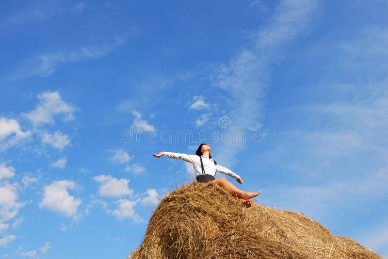 Woman on hay bale in summer field enjoying a warm windy day