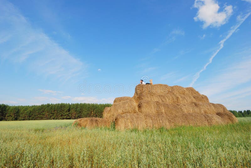 Woman on hay bale in summer field enjoying a warm windy day