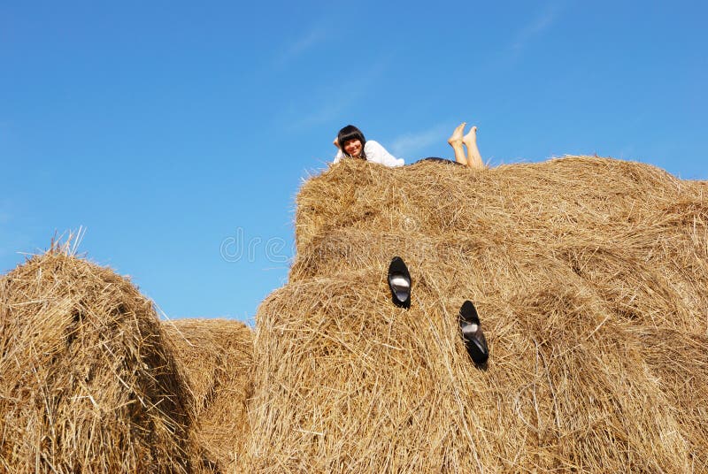 Woman on hay bale in summer field enjoying a warm windy day