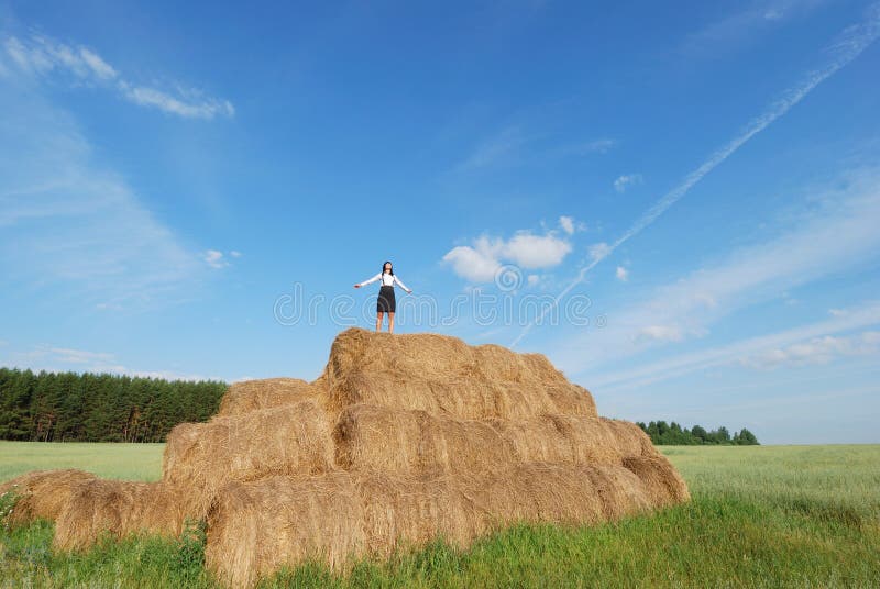 Woman on hay bale in summer field enjoying a warm windy day