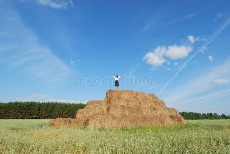 Woman on hay bale in summer field enjoying a warm windy day