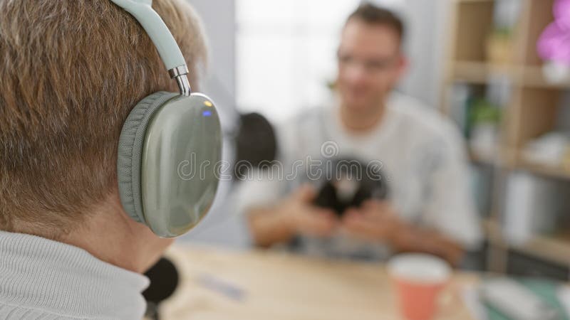 A woman with headphones interviews a blurred man on a podcast in a studio, creating a dynamic interactive scene royalty free stock photography