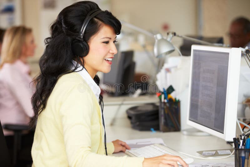 Woman with Headset Working at Desk in Busy Creative Office Stock Photo