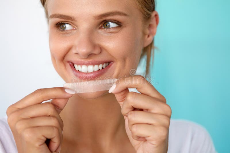 Healthy White Teeth. Beautiful Smiling Girl Holding Teeth Whitening Strip. Happy Young Woman With Perfect White Smile Using Dental Whitener. Dental Beauty, Tooth Care Concept. High Resolution Image. Healthy White Teeth. Beautiful Smiling Girl Holding Teeth Whitening Strip. Happy Young Woman With Perfect White Smile Using Dental Whitener. Dental Beauty, Tooth Care Concept. High Resolution Image