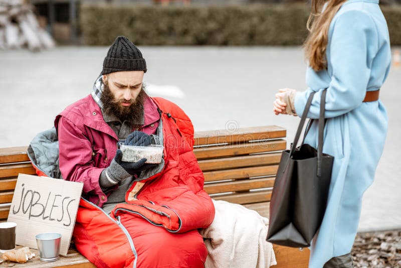 Woman giving food to a homeless beggar. Woman helping homeless beggar giving some food outdoors. Concept of helping poor people stock image Woman giving food to a homeless beggar. Woman helping homeless beggar giving some food outdoors. Concept of helping poor people stock image