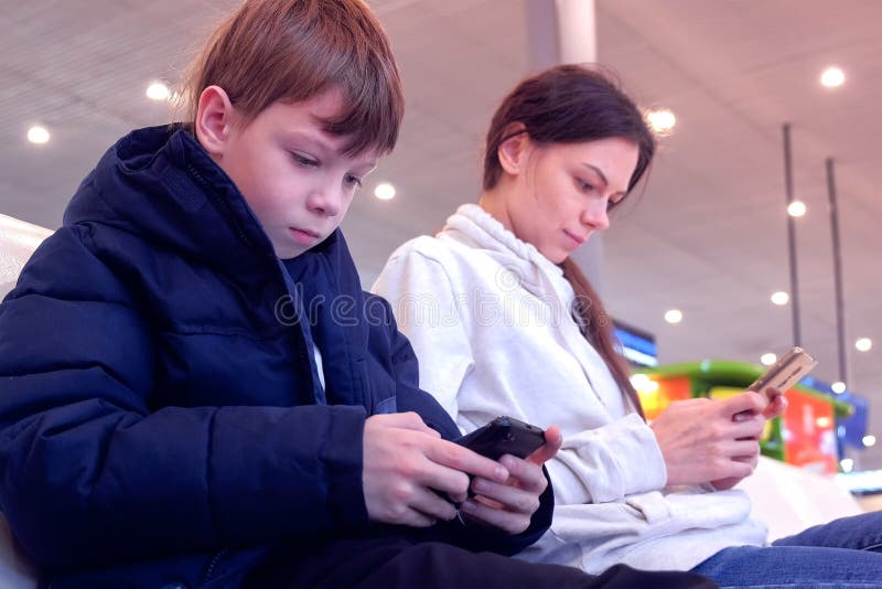 Woman with her son browsing on mobile phones in airport hall waiting for flight. royalty free stock photo Woman with her son browsing on mobile phones in airport hall waiting for flight. royalty free stock photo