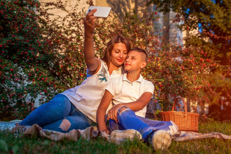 Woman with her teenager son taking selfie on smartphone. Happy family spending time outdoors sittting on grass in park. royalty free stock image Woman with her teenager son taking selfie on smartphone. Happy family spending time outdoors sittting on grass in park. royalty free stock image