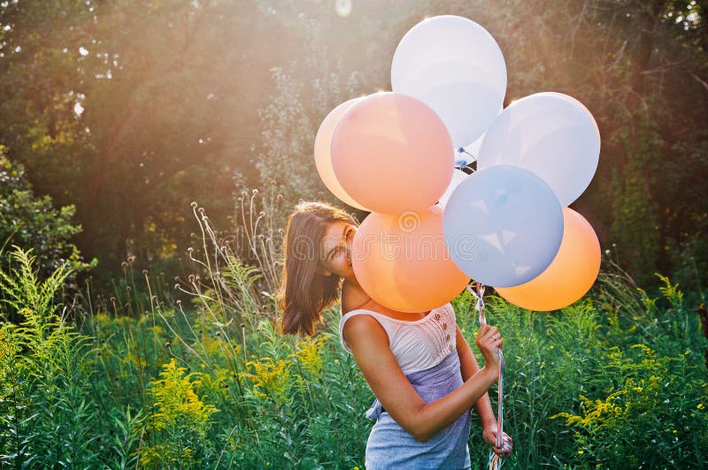 Smiley woman in a white shirt and blue skirt is holding colored baloons. Smiley woman in a white shirt and blue skirt is holding colored baloons