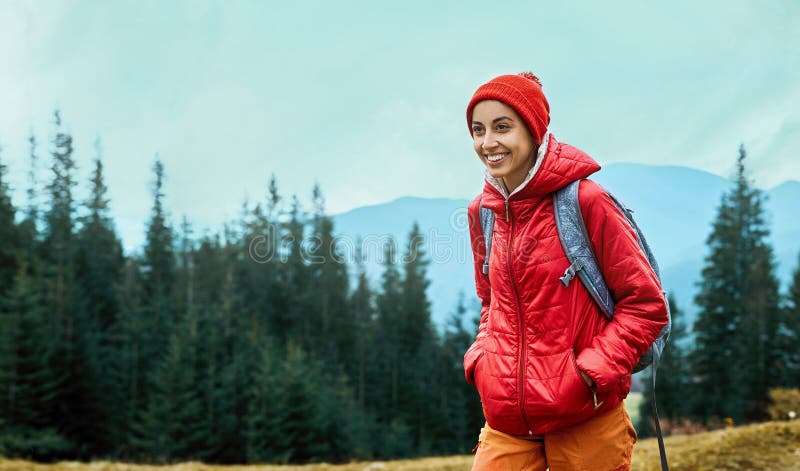 Woman hiker with small backpack wearing in red jacket and orange pants walks by trail through pine woods in the royalty free stock photography Woman hiker with small backpack wearing in red jacket and orange pants walks by trail through pine woods in the royalty free stock photography