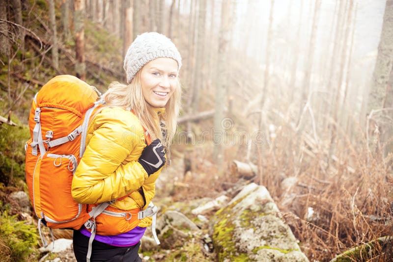 Woman hiking in autumn forest in mountains. Trekking, recreation and healthy lifestyle outdoors in nature. Beauty blond backpacker looking at camera smiling, bright light sunlight in background. Woman hiking in autumn forest in mountains. Trekking, recreation and healthy lifestyle outdoors in nature. Beauty blond backpacker looking at camera smiling, bright light sunlight in background.