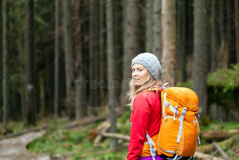 Woman hiking on trail in forest. Recreation and healthy lifestyle outdoors in nature. Beauty blond hiker with backpack looking at camera. Woman hiking on trail in forest. Recreation and healthy lifestyle outdoors in nature. Beauty blond hiker with backpack looking at camera.