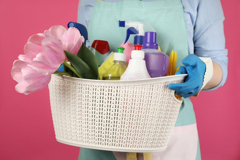 Woman holding basket with spring flowers and cleaning supplies on background, closeup