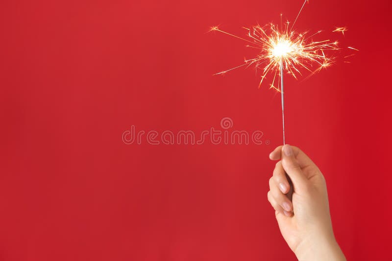 Woman holding bright burning sparkler on red background, closeup. Space for text
