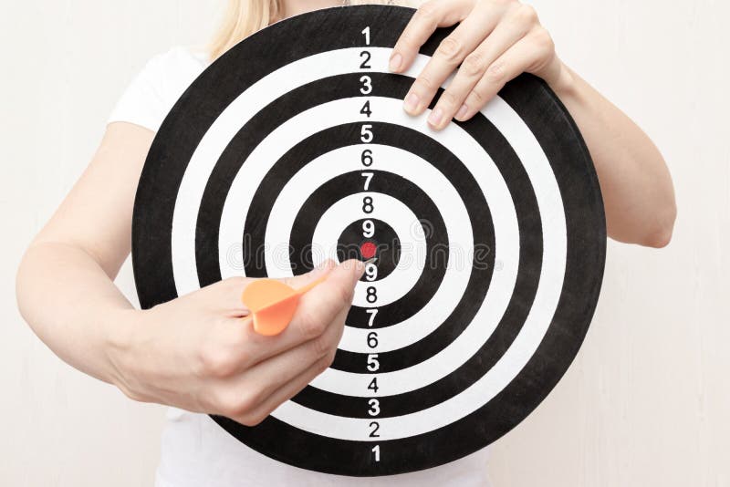 Woman holding a dart board and darts in hands close up, aiming and targetting in business and life concept