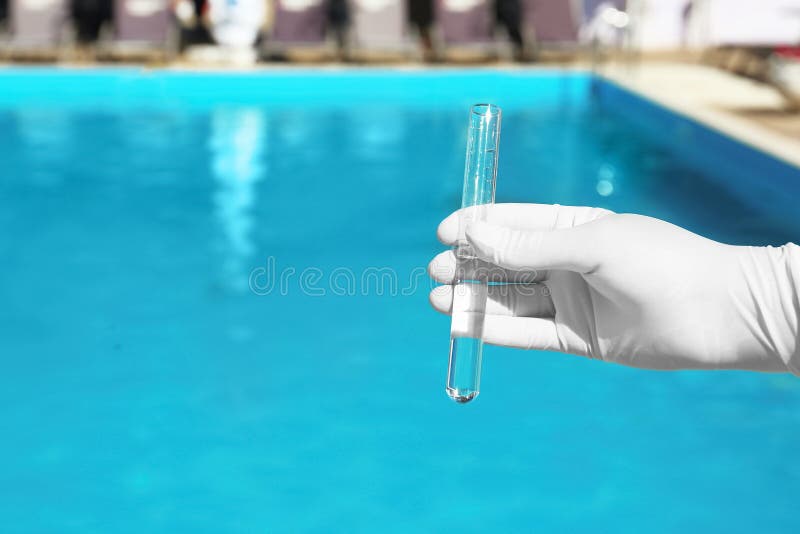 Woman holding glass tube with sample of  pool water to check PH level outdoors, closeup