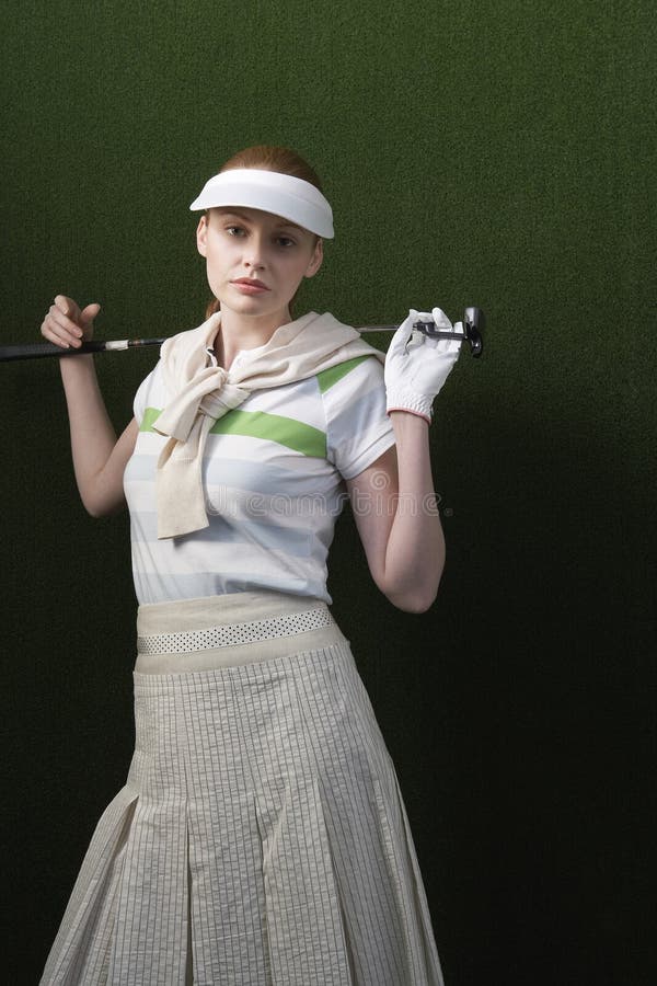 Portrait of serious young woman holding golf club behind shoulders against green background